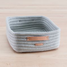 a gray basket with leather handles on a wooden table