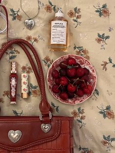 a red purse sitting on top of a bed next to a bowl of cherries