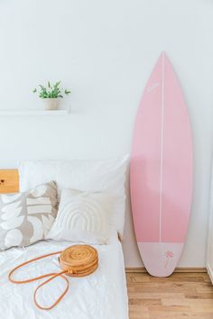 a pink surfboard sitting on top of a bed next to a pillow and blanket