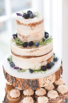 a three tiered wedding cake with fresh berries and blueberries on the top is surrounded by cupcakes