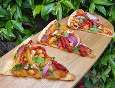 three slices of pizza on a wooden cutting board in front of green leaves and bushes