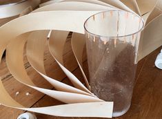 a glass filled with liquid sitting on top of a wooden table next to paper and scissors