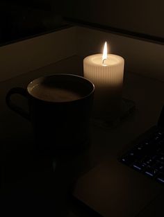 a lit candle sitting on top of a table next to a cup of coffee and a laptop computer