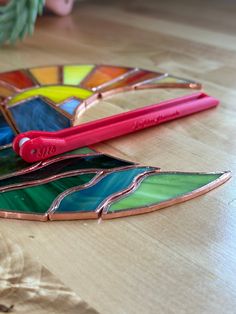 a colorful stained glass piece with a pink toothbrush next to it on a wooden table