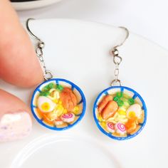 a pair of earrings with food in the middle on top of a white plate next to a person's finger