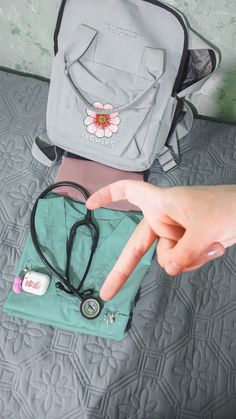 a person pointing at something on top of a bed next to a backpack and stethoscope