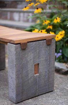 a bench made out of concrete and wood sitting in front of some yellow daisies