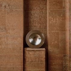 a metal object sitting on top of a block of cement next to a wall covered in brown tiles