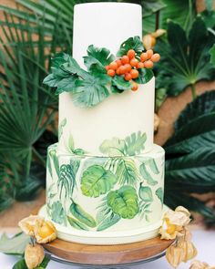 a white and green wedding cake with orange berries on top, surrounded by greenery