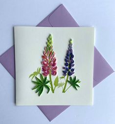 a card with two flowers on it sitting next to an envelope and purple envelope paper