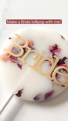 a bride lollipop with the word bride spelled in gold on it and flowers