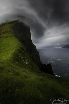 a green grassy hill next to the ocean on a cloudy day with dark clouds in the sky