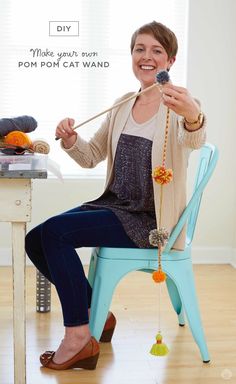 a woman sitting on a blue chair holding a beaded necklace and smiling at the camera