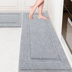 a person standing on a rug in the middle of a kitchen with white walls and flooring