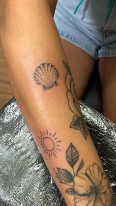 a woman's arm with flowers and shells tattoo on her left arm, while the sun shines in the background