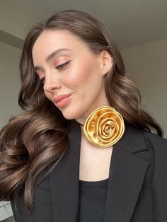 a woman with long hair wearing a black blazer and gold flower earrings on her neck