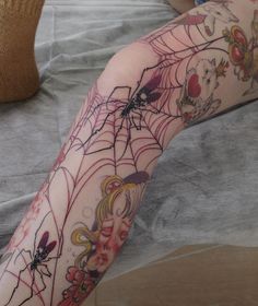 a spider web tattoo on the leg of a woman's arm with flowers and leaves