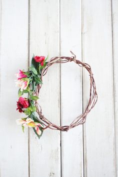 a wreath made out of branches with flowers and leaves around it on a white wooden surface