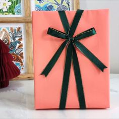 a pink gift box with a green ribbon on it sitting on a table next to pictures