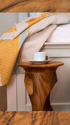 a wooden table sitting next to a bed with a blanket on top of it and a cup in the middle