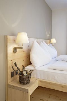 a bed with white sheets and pillows next to a basket on a wooden night stand