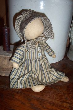 an old fashioned doll sitting next to a potted plant on a wooden floor in front of a white vase