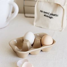 three eggs in a carton on a table next to a coffee cup and bag