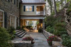 a stone house with steps leading to the front door and covered patio area, surrounded by greenery