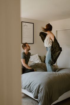 a man standing on top of a bed next to a woman sitting on the bed