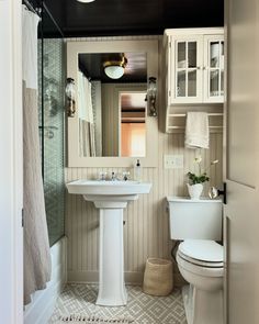 a white toilet sitting next to a sink in a bathroom under a mirror and lights