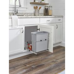 a kitchen with white cabinets and wood flooring, an open trash can is in the corner