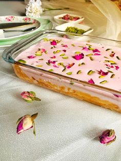 a cake with pink frosting in a glass dish on a table next to flowers