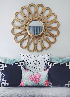 a bed topped with lots of pillows next to a wall mounted round mirror on the wall