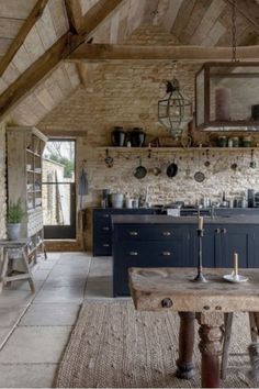 an old fashioned kitchen with stone walls and wooden ceilinging, blue cabinets and stools