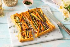 a vegetable tart on a plate with a knife next to it and flowers in the background