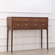 a wooden table with two drawers and gold knobs on the bottom, against a white wall