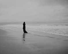 black and white photograph of a woman standing on the beach looking out at the ocean