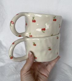 two coffee mugs with cherries on them are held in the air by someone's hand