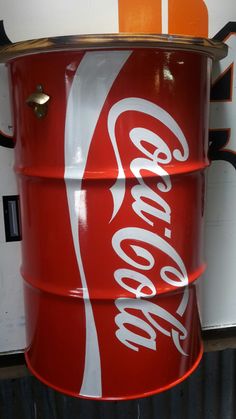 a red and white coca cola can sitting on top of a metal shelf next to a wall