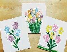 three cards with flowers painted on them sitting next to each other in front of a wooden table