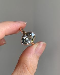 a woman's hand holding a ring with an oval shaped diamond on it, in front of a gray background