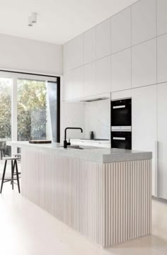 a kitchen with an island counter and stools in front of large windows overlooking the backyard