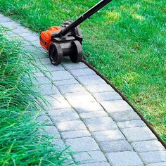 a lawn mower sitting on the side of a brick walk way next to green grass