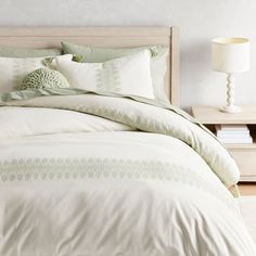 a bed with white and green comforters in a bedroom next to a night stand