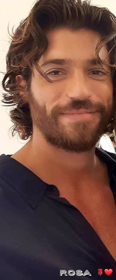 a man with long curly hair and beard smiling at the camera while wearing a black shirt