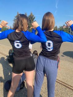 two women in blue and black shirts standing next to each other with their hands on their hips