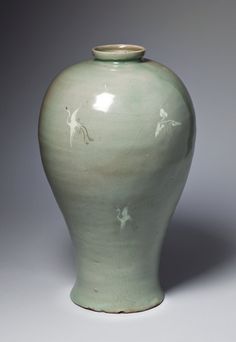 a green vase sitting on top of a white table next to a gray wall with birds painted on it