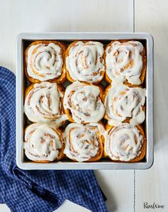 a pan filled with cinnamon rolls sitting on top of a blue cloth next to a napkin