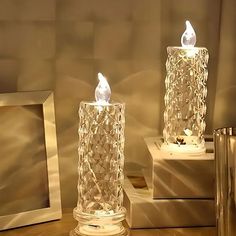 two clear glass candles sitting next to each other on top of a wooden table in front of a mirror