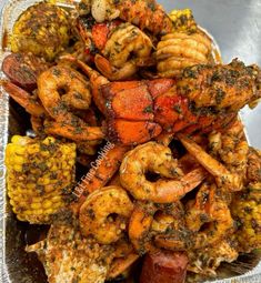 cooked shrimp and corn on the cob with seasoning in a foil container, ready to be eaten